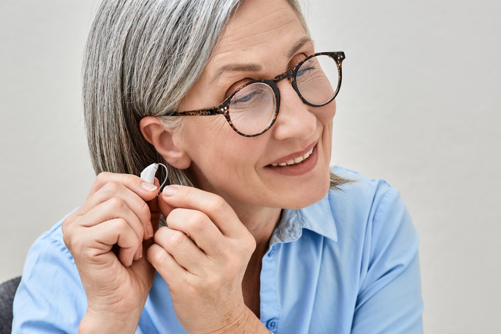 Grey Haired Mature Woman With Hearing Impairment Using Hearing Aid. Hearing Solutions For Deafness People